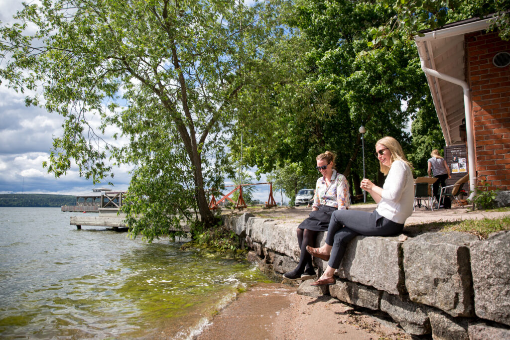 kaksi naista istuu kiveyksellä järven rannassa