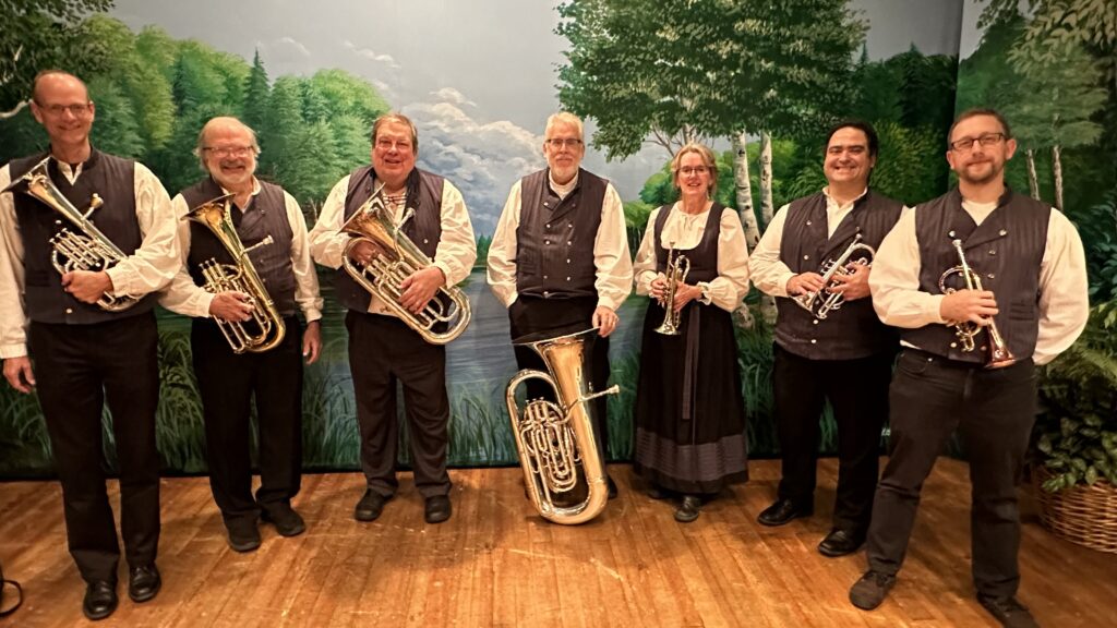 Seitsemän soittajaa hymyilee soittimineen puolikaaressa kansallispukuhenkisisssä vaatteissa.