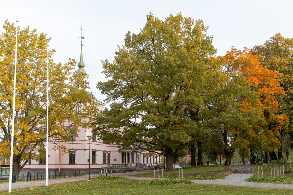 Vaaleanpunainen kartanorakennus koristeellisine torneineen syksyn punaisten ja keltaisten puiden takana.